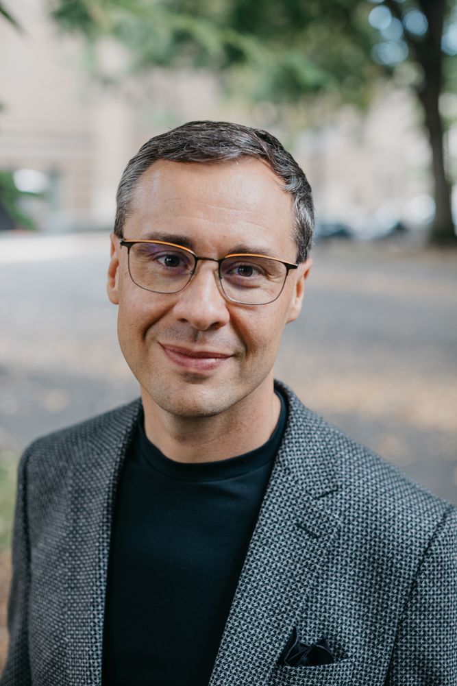 Headshot of Joshua Berry smiling, in a grey blazer and black shirt