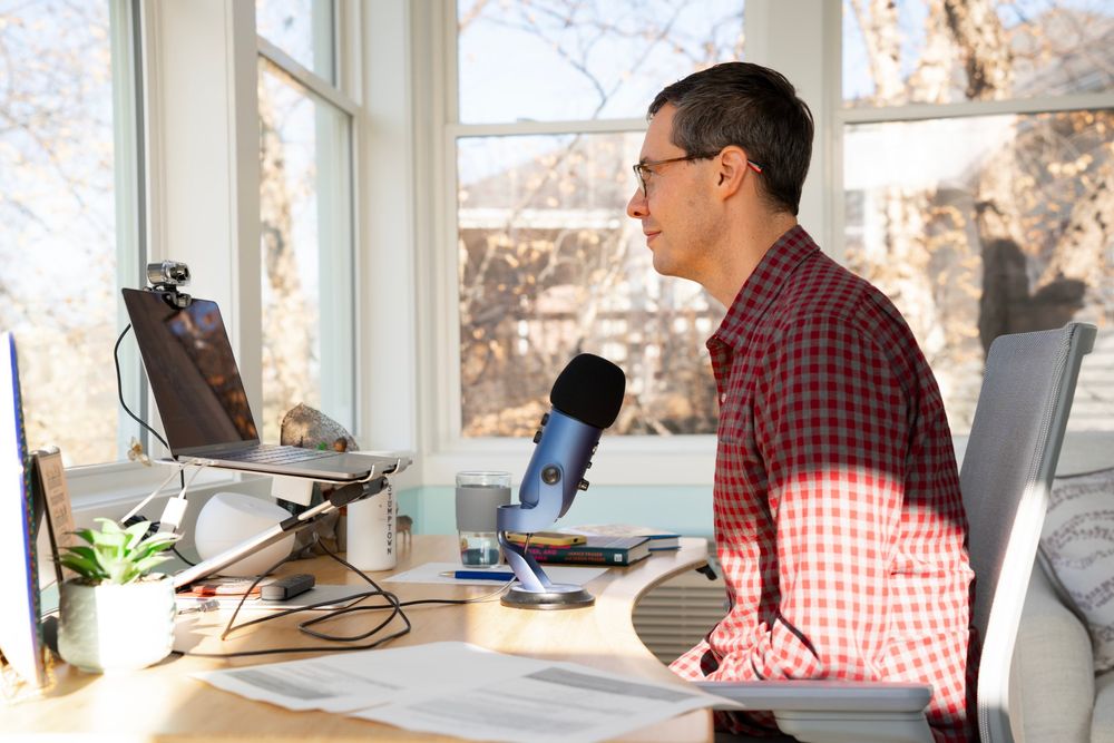 Joshua Berry at his desk speaking into a podcast microphone, in a red checked shirt
