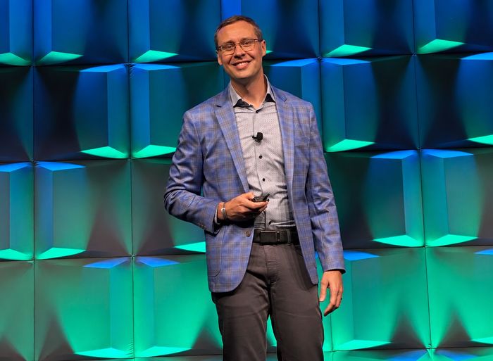 Joshua Berry smiling on stage in a blue plaid jacket, holding a presentation clicker