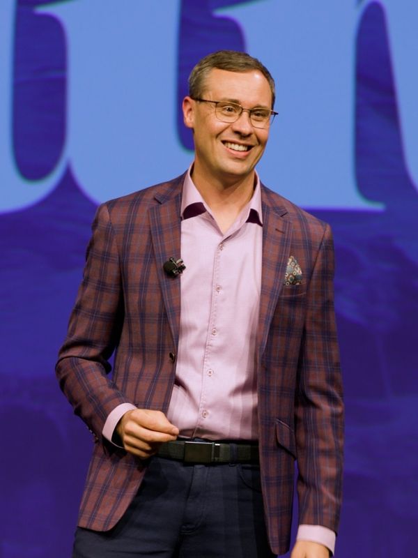 Joshua Berry smiling on stage in a plaid jacket, in front of a bright blue presentation screen